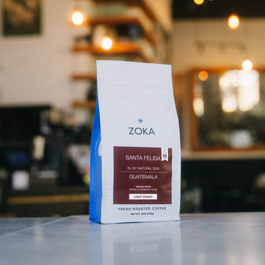 A bag of ZOKA Santa Felisa coffee on a countertop in a blurred cafe setting.