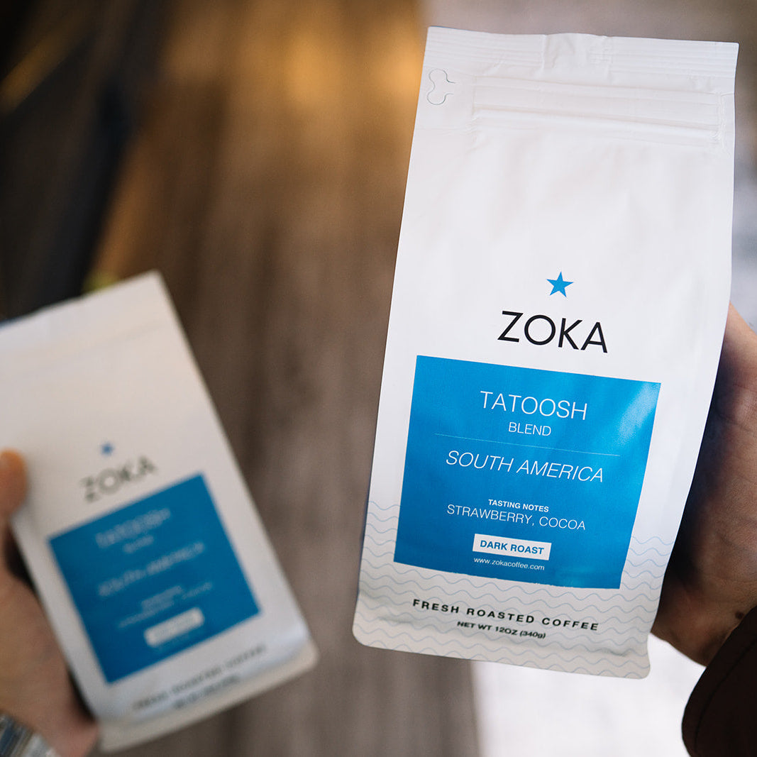 Comparing two bags of Zoka 12 oz coffee beans, one in each hand.
