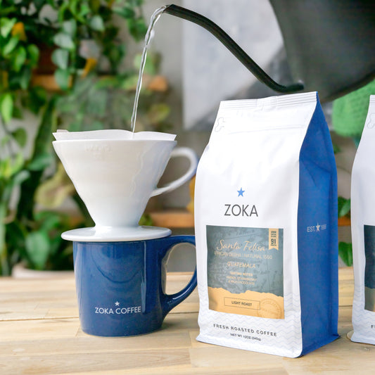 Zoka Coffee bags with a pour-over coffee setup on a wooden table.
